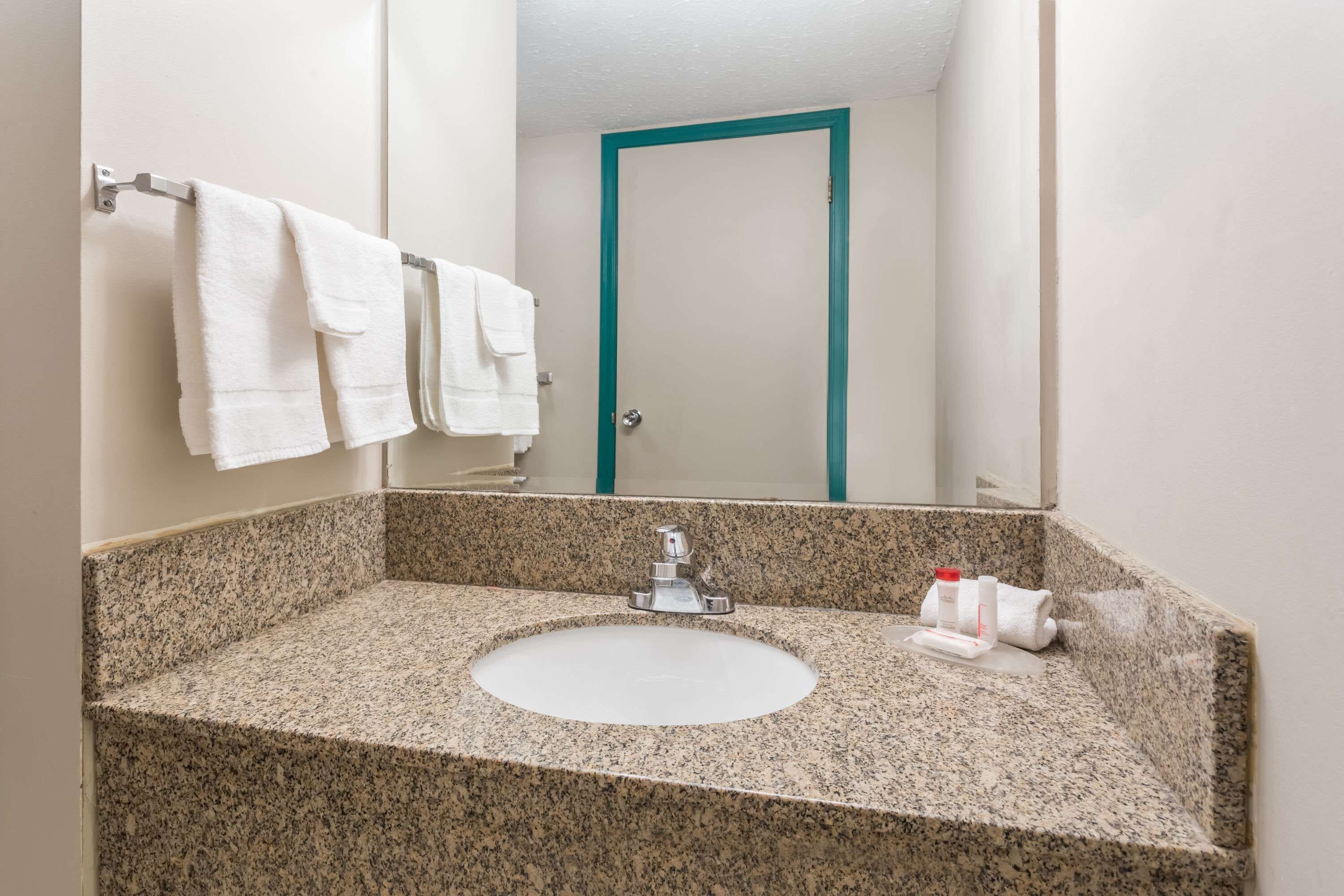 Un baño con lavamanos de encimera de granito, un espejo y una puerta con detalles en color turquesa.