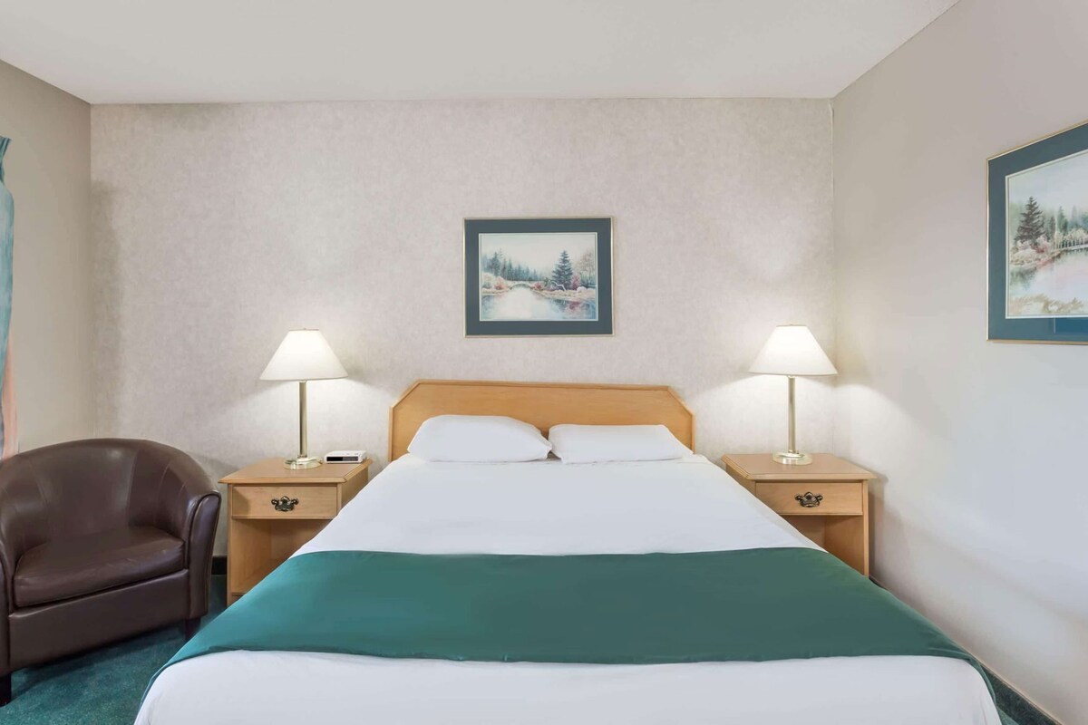 A hotel room with a bed, two bedside tables with lamps, a chair, and two framed pictures on the walls.