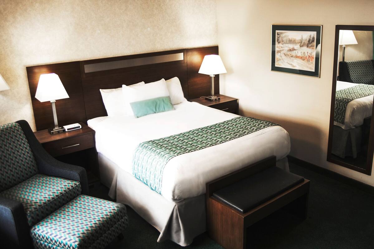 Habitación de hotel con una cama grande, dos lámparas de noche, una silla, un banco y dos cuadros en la pared.