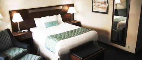 Habitación de hotel con una cama grande, dos lámparas de noche, una silla, un banco y dos cuadros en la pared.