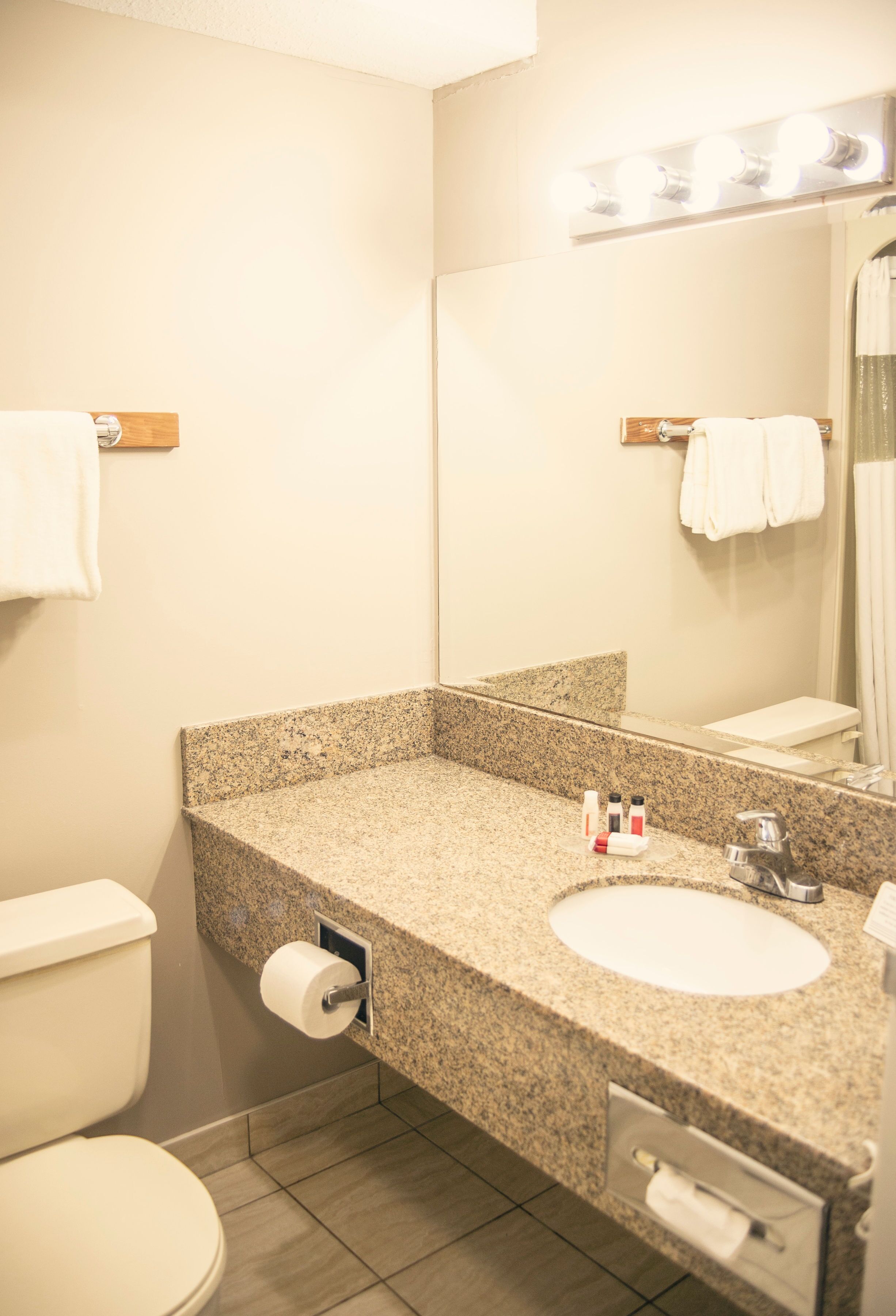 A bathroom with a granite countertop sink, a mirror, and a toilet.