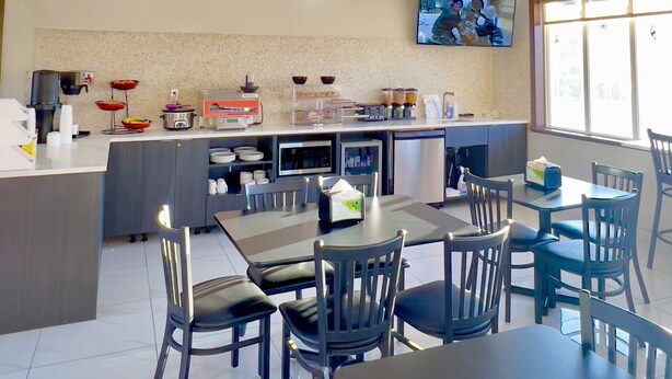 A modern kitchen with a dining area, equipped with a coffee machine, microwave, and refrigerator. - Ramada by Wyndham Quesnel (Quesnel)