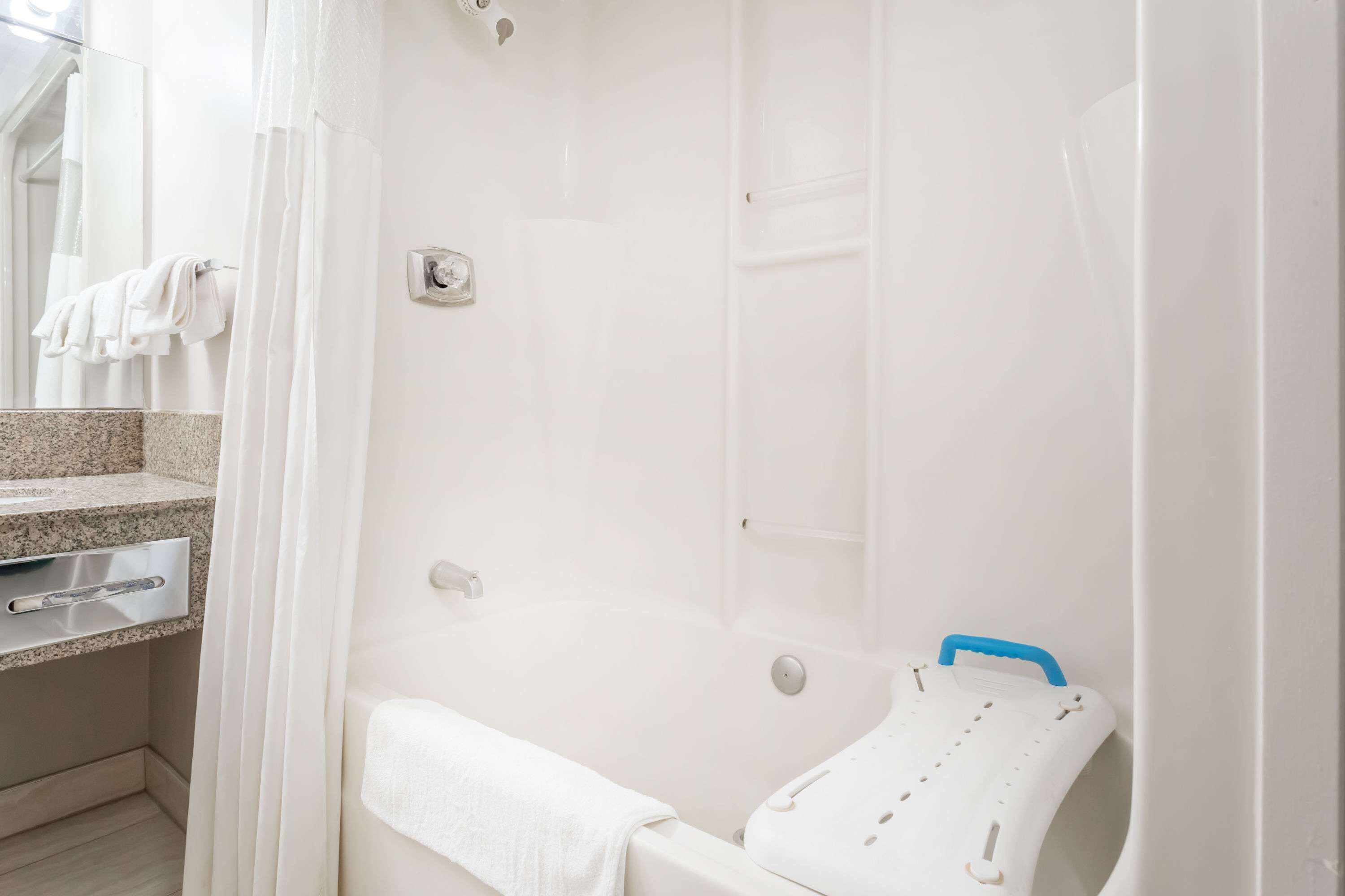 A bathroom with a bathtub, a shower curtain, a towel rack, and a small white stool.