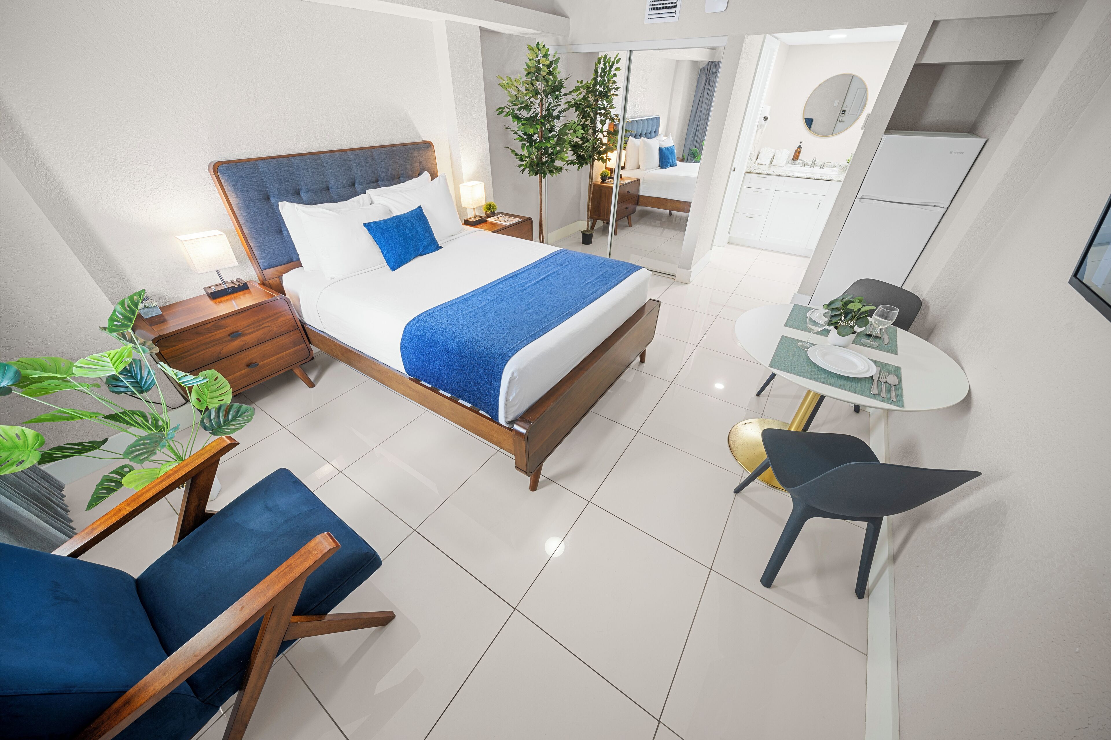 A modern hotel room with a large bed, a desk, a chair, and a small dining table.