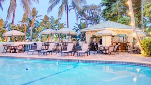 Ein Poolbereich mit Liegestühlen, Sonnenschirmen, einer Bar und Palmen.