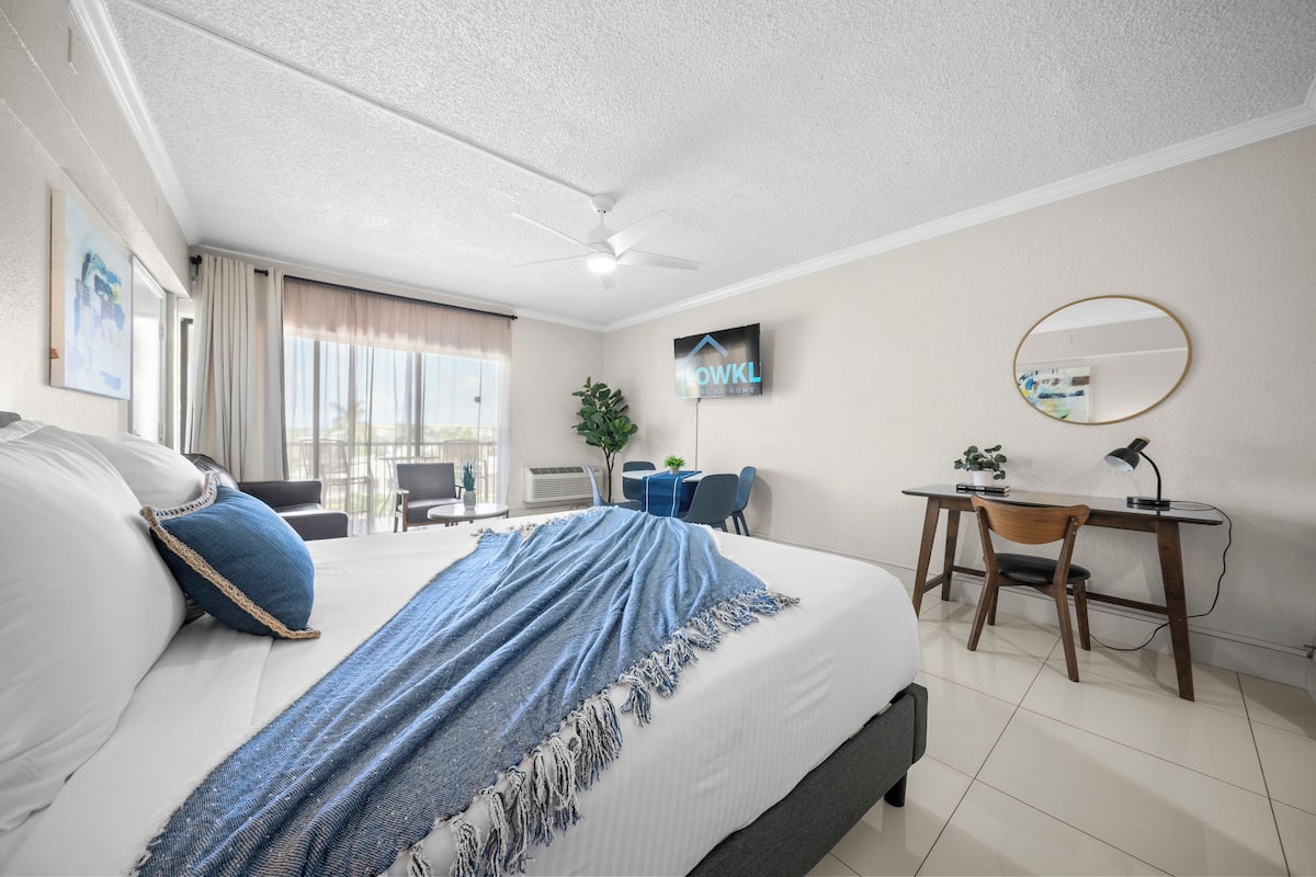 A hotel room with a bed, a desk, a chair, a TV, and a ceiling fan.
