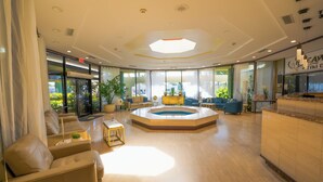 A spacious lobby with a central seating area, a reception desk, and large windows offering views of the outdoors. - Boca Plaza by Lowkl (Boca Raton)