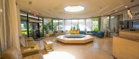 A spacious lobby with a central seating area, a reception desk, and large windows offering views of the outdoors.