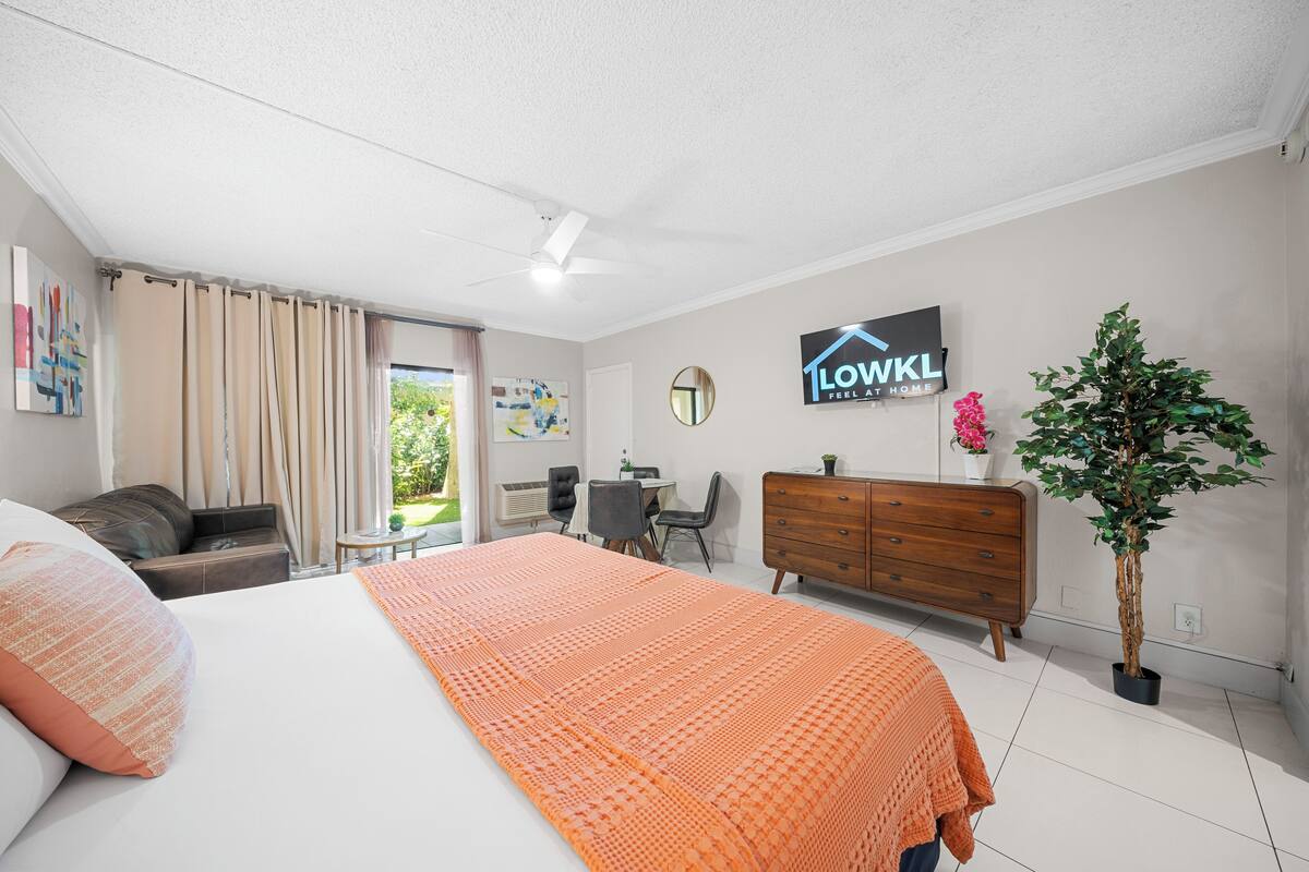 A bedroom with a large bed, a dresser, a desk, and a potted plant.