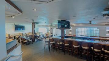 Un área de bar moderna con una barra larga, varios taburetes y un televisor montado sobre la barra.