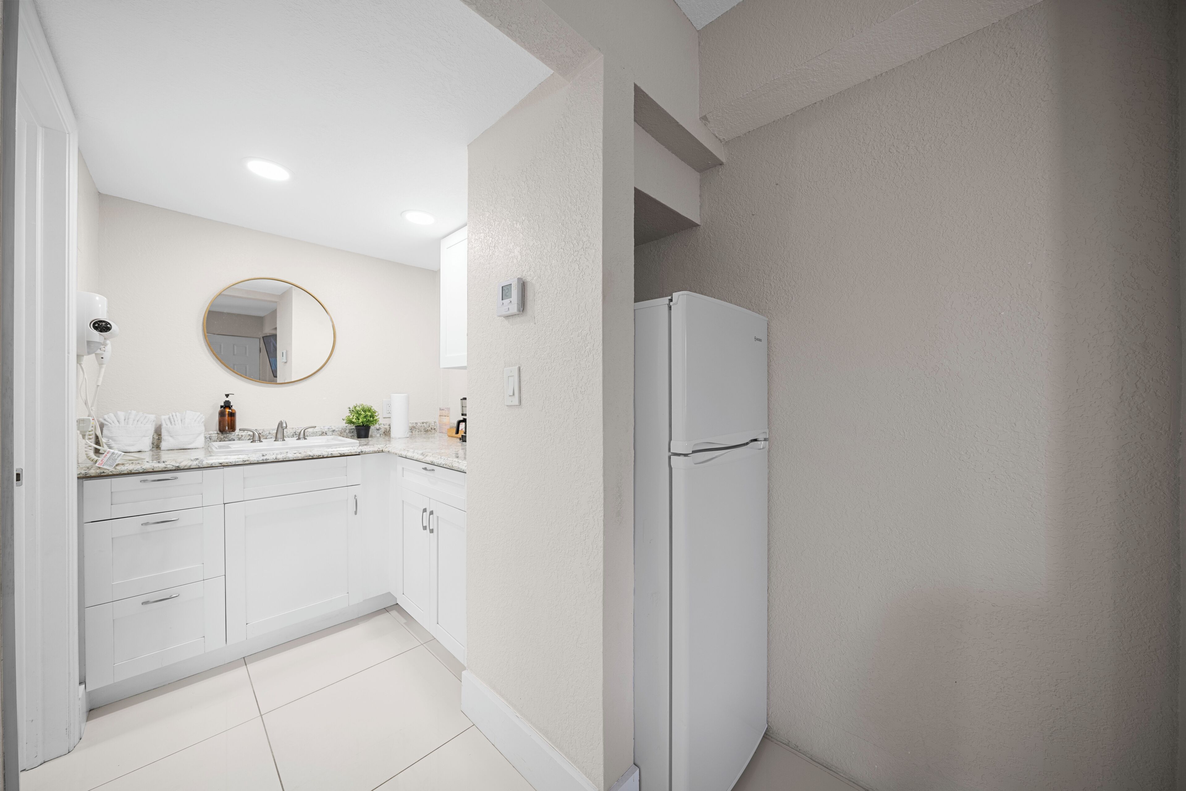 A modern kitchen with white cabinets, a white refrigerator, a round mirror, and a built-in oven.