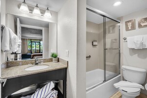 Un baño con lavamanos de encimera de granito, un espejo, una planta en maceta y cabina de ducha con mampara de cristal.