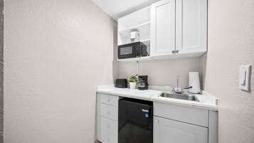 A compact kitchenette with white cabinets, a microwave, a coffee maker, a sink, and a dishwasher.