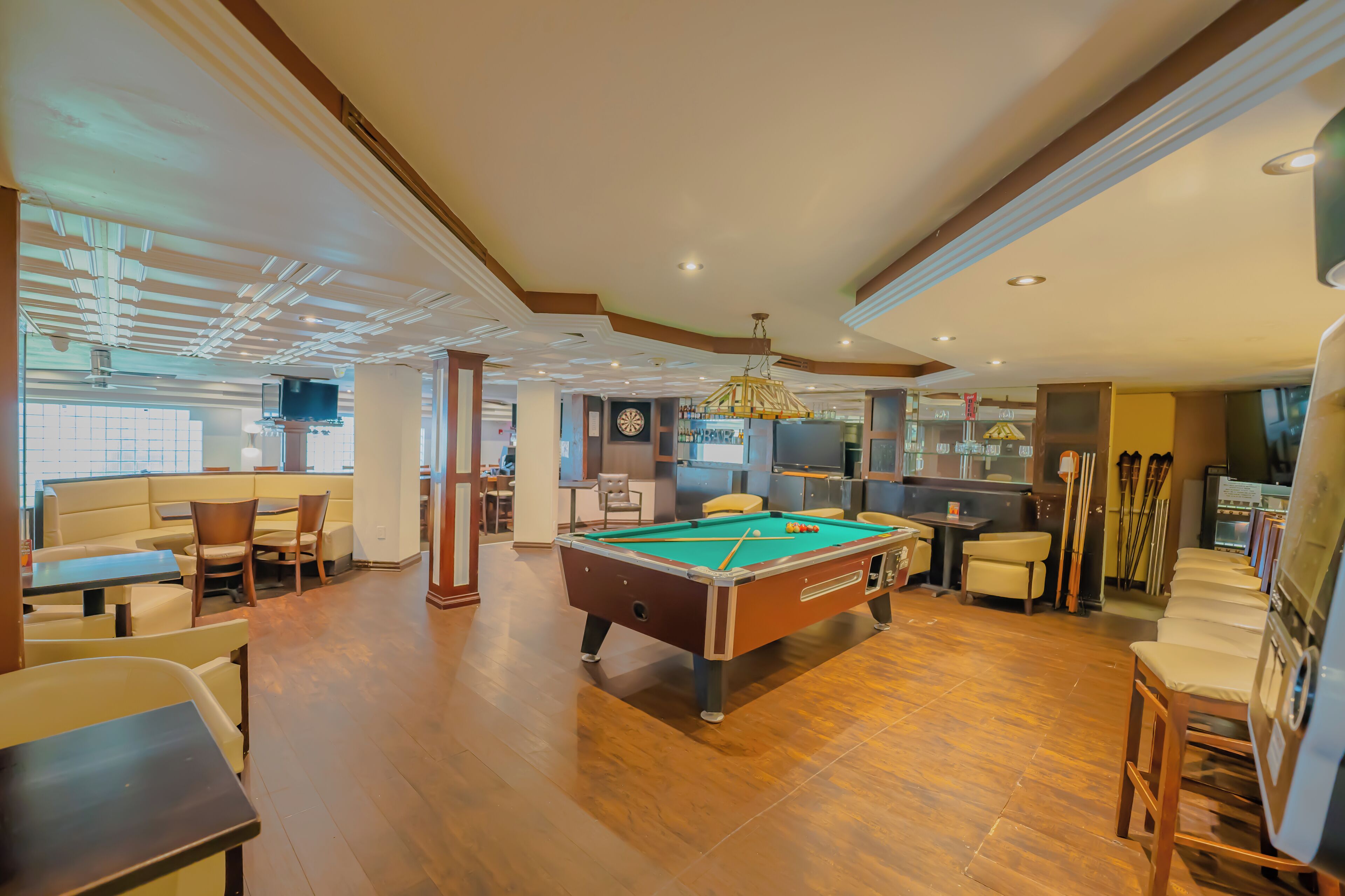 A pool table in a well-lit room with wooden flooring, a sofa, and a television in the background.