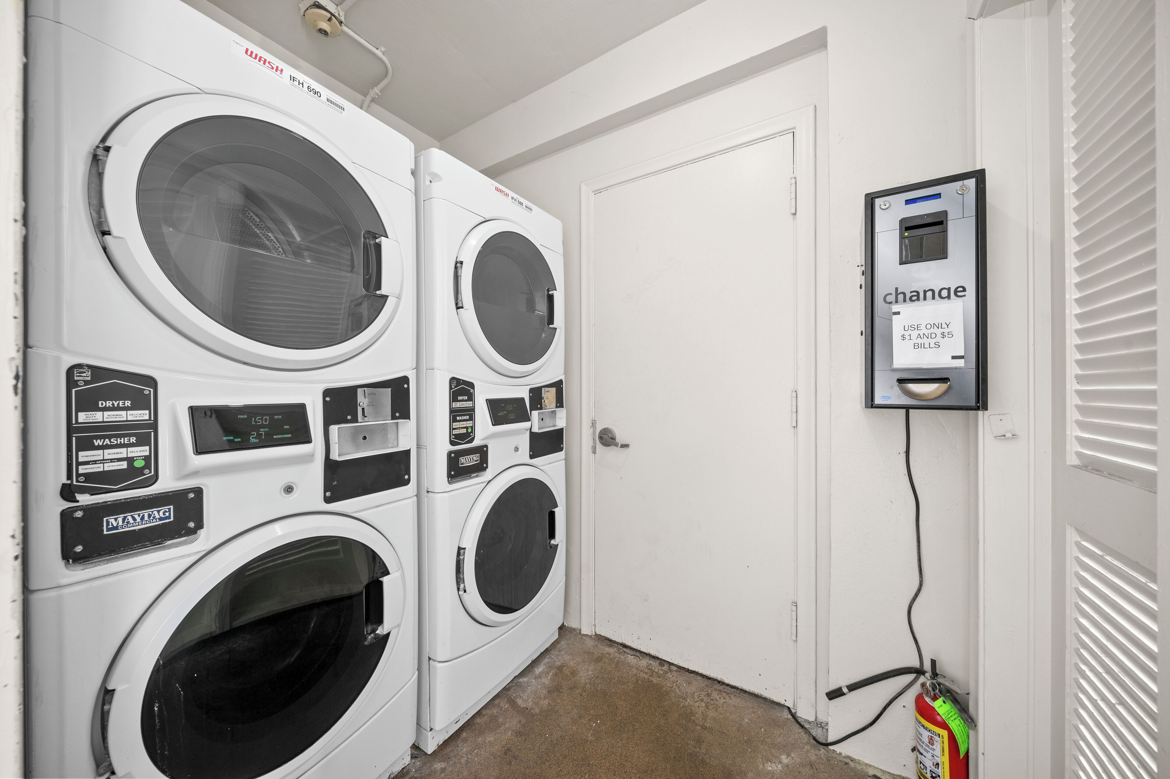 Une buanderie équipée de deux machines à laver et deux sèche-linge Maytag, d’un appareil pour la vente de pièces de monnaie et d’un extincteur.
