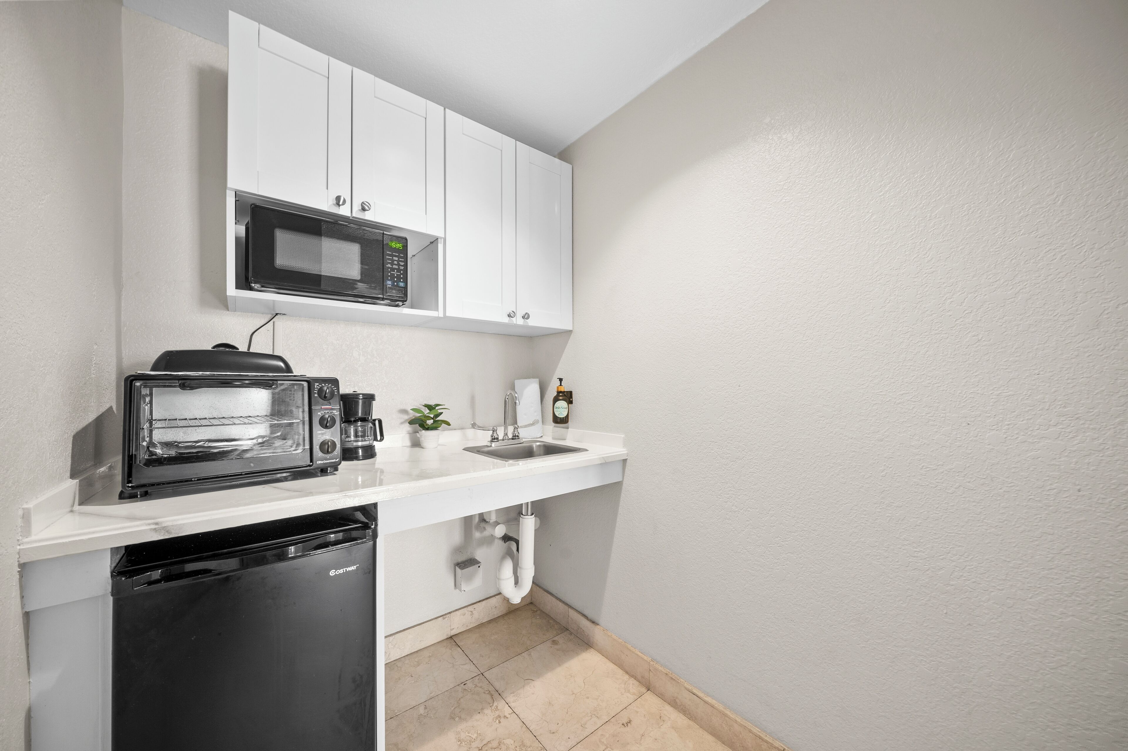 A compact kitchen with white cabinetry, a built-in microwave, a toaster oven, and a dishwasher.