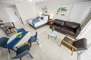 Una habitación de hotel moderna con una cama, un sofá de cuero marrón, una mesa de comedor con sillas y una pequeña planta en maceta.
