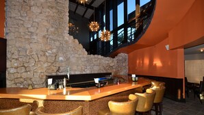 A bar area with a stone wall, bar counter, and several bar stools.