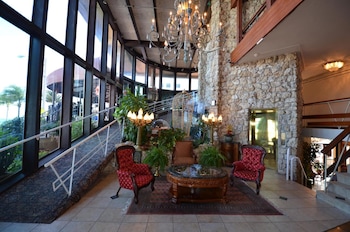 Step into a grand lobby with a high ceiling, stone wall, and large window offering a view of the outdoors. at Sea Club Resort