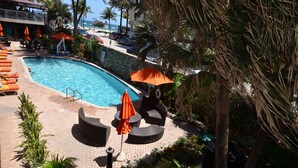 A pool area with lounge chairs and umbrellas, surrounded by palm trees and a stone wall.