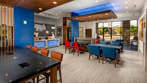 A modern indoor space with a black conference table, red and blue chairs, a seating area with a blue sofa, and a view of the outdoors through large windows. - Holiday Inn Express & Suites Chatsworth by IHG (Chatsworth)