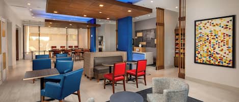 A modern hotel lobby with seating areas, a fireplace, and a colorful abstract painting.