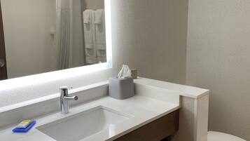 A modern bathroom with a large mirror, a white sink, a towel rack, and a toilet.