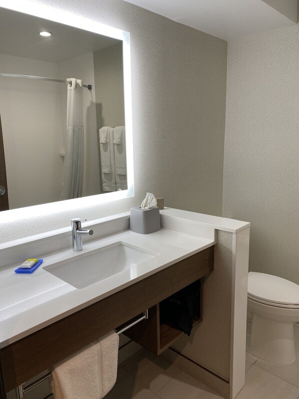 A modern bathroom with a large mirror, a white sink, a towel rack, and a toilet.