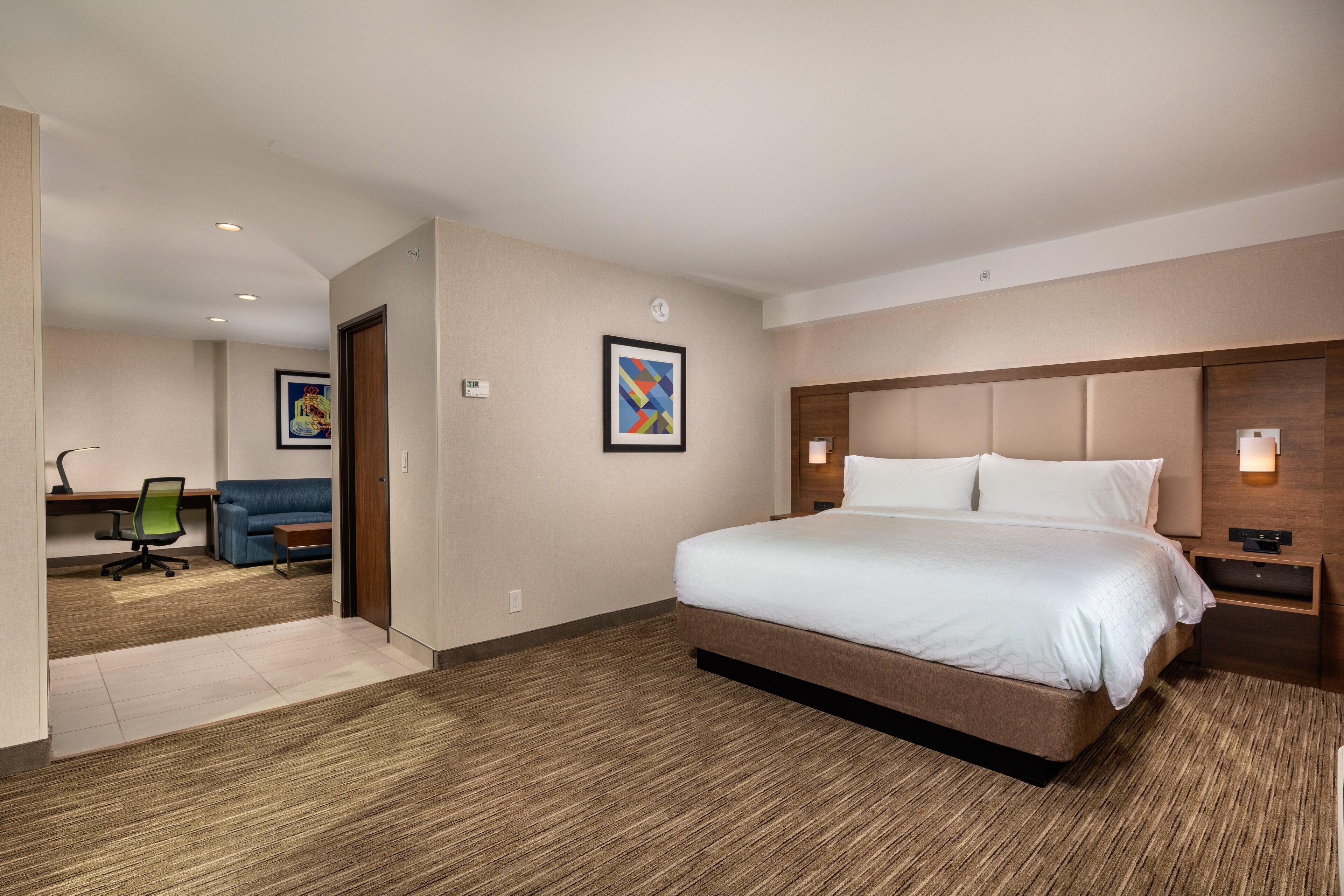 A hotel room with a large bed, a desk with a chair, a sofa, and two wall-mounted light fixtures.