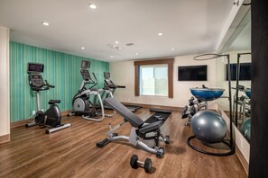 Un gimnasio con máquinas de cardio, banco de pesas, mancuernas y una pelota de ejercicio grande.