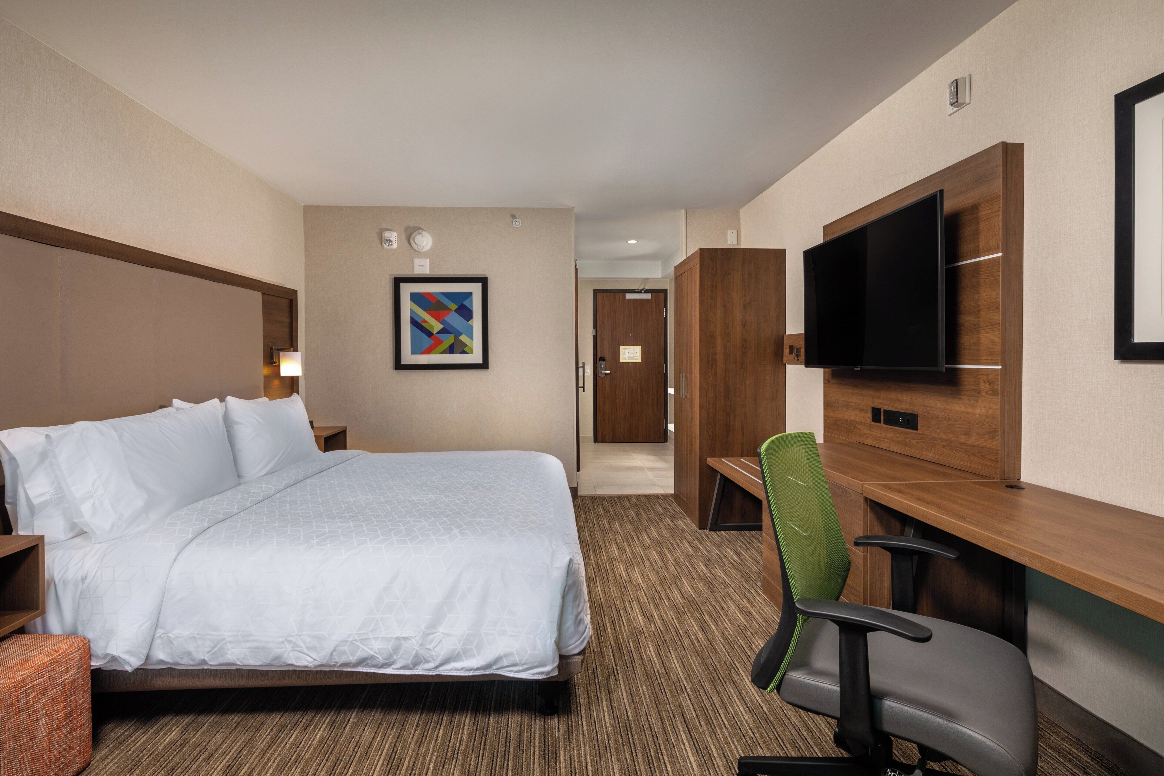A hotel room with a bed, a desk, a chair, a television, and a framed picture on the wall.