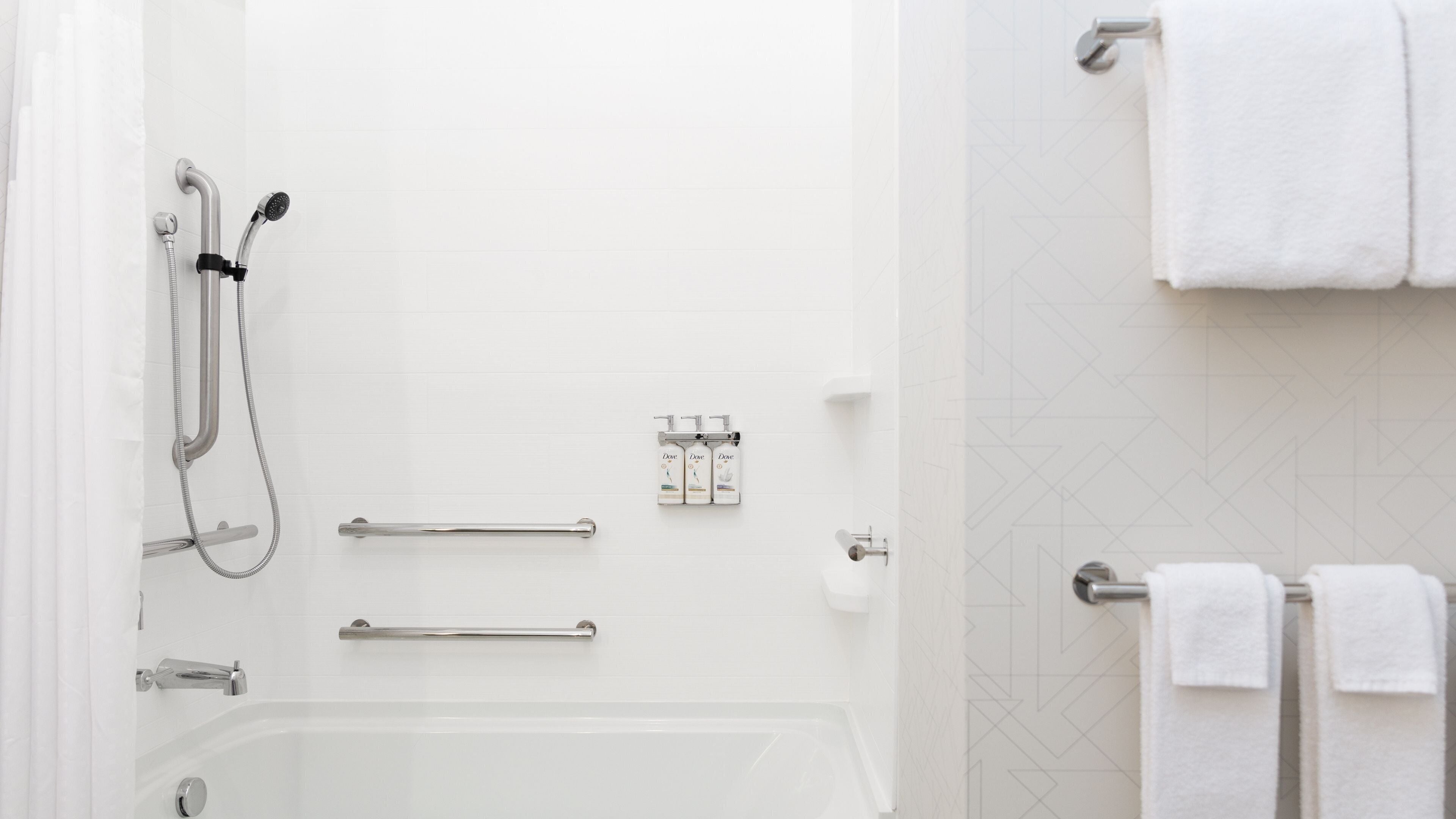 A modern bathroom with a bathtub, shower, and handrails.