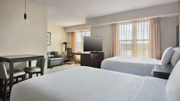 A hotel room with a large bed, a desk, a chair, a television, and a window with curtains.