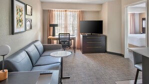 Ein Hotelzimmer mit einer Couch, einem kleinen Tisch, einem Fernseher, einem Schreibtisch mit Stuhl und einem Bett.