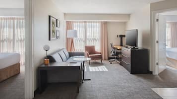 A hotel room with a bed, a sofa, a desk, a chair, a TV, and a lamp.