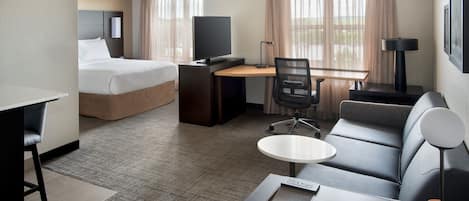 A hotel room with a bed, desk, chair, sofa, and a small table.
