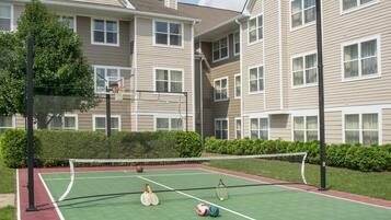An outdoor tennis court with a net, tennis rackets, and a ball.