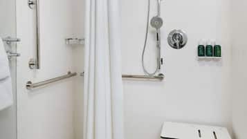 A modern bathroom with a walk-in shower, grab bars, a white sink, and a small table.