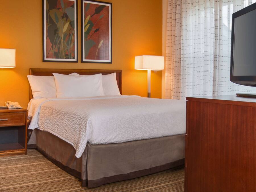 Habitación de hotel con cama, dos lámparas de noche, televisor y mesita de noche con teléfono.