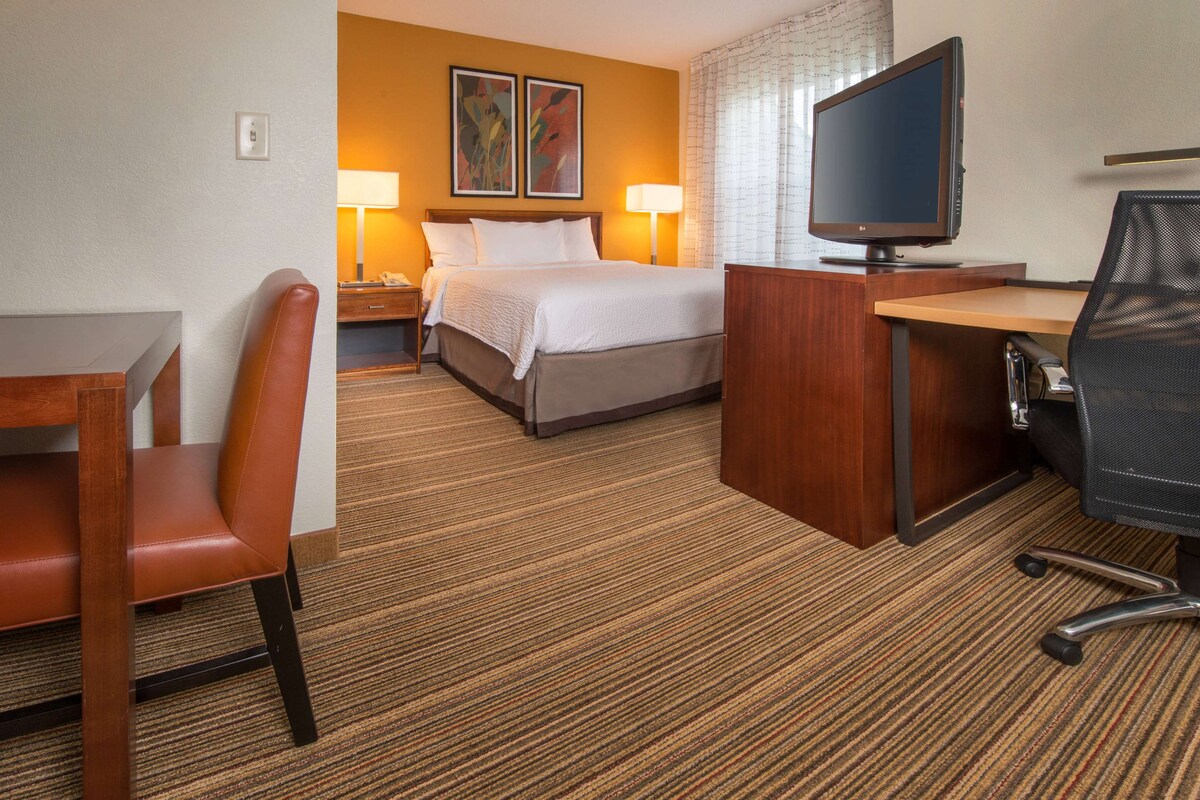 A hotel room with a bed, desk, chair, TV, and lamps.