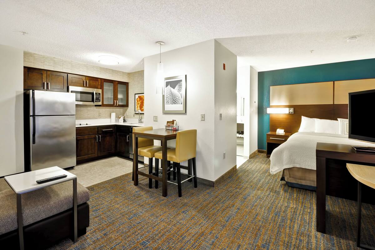 A hotel room with a kitchenette, a dining area, a bed, and a TV.