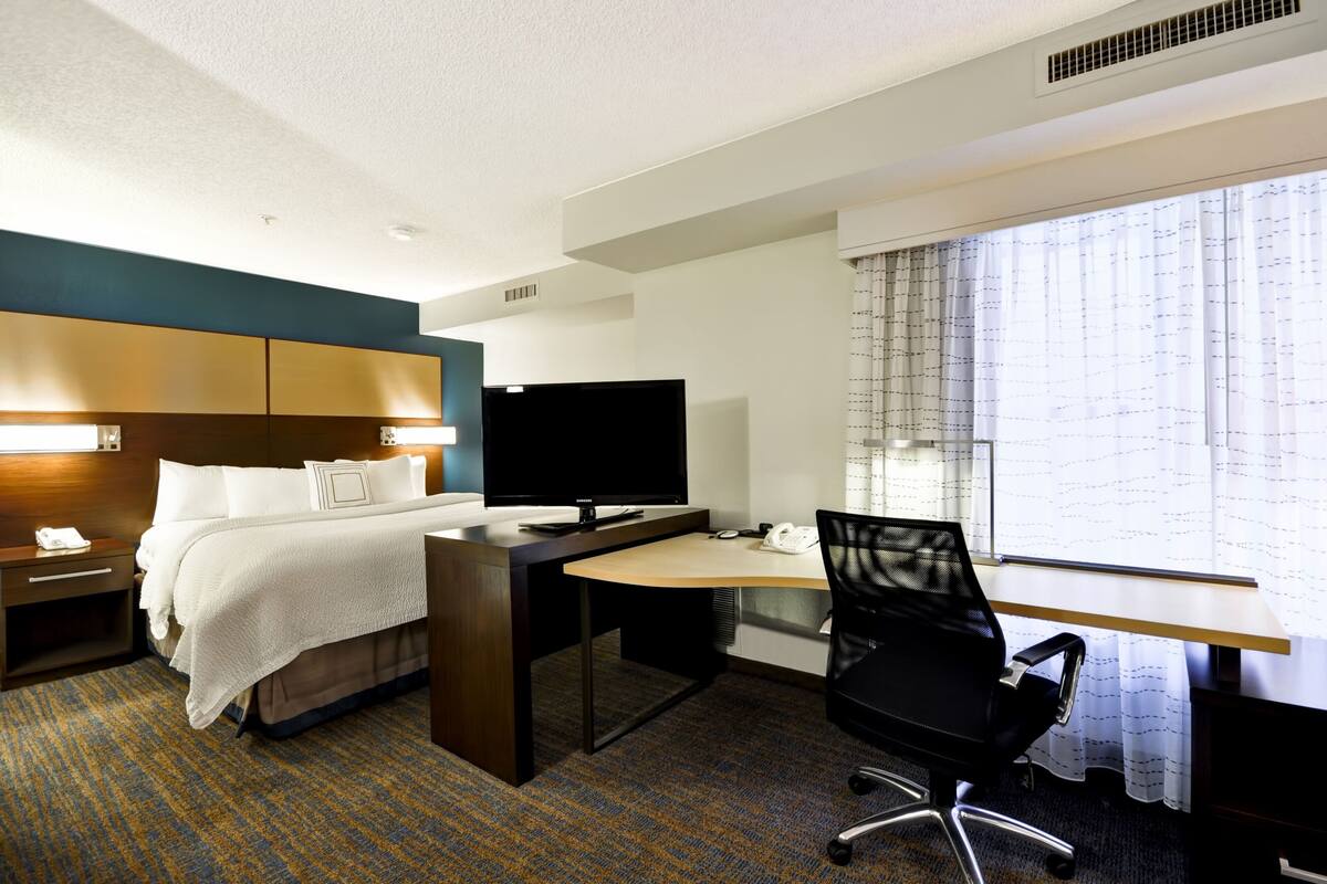 A hotel room with a bed, desk, chair, TV, and window with curtains.
