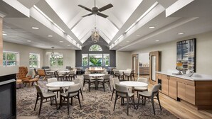 A spacious dining area with round tables and chairs, a ceiling fan, and large windows allowing natural light. - Residence Inn by Marriott Orlando East/UCF Area (Orlando)