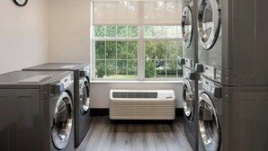 A laundry room with two front-loading washers, a dryer, and a window with a view of trees. - Residence Inn by Marriott Orlando East/UCF Area (Orlando)