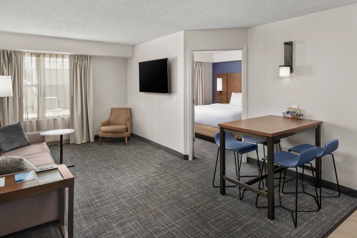 A hotel room with a bed, a desk with chairs, a TV, and a window with curtains.
