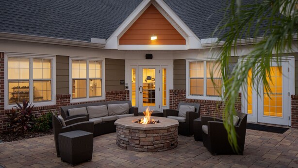 A patio area with a stone fire pit, outdoor furniture, and a brick exterior. - Residence Inn by Marriott Orlando East/UCF Area (Orlando)