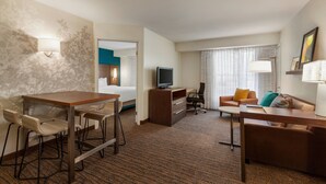 Habitación de hotel con comedor, sofá, televisor y escritorio.