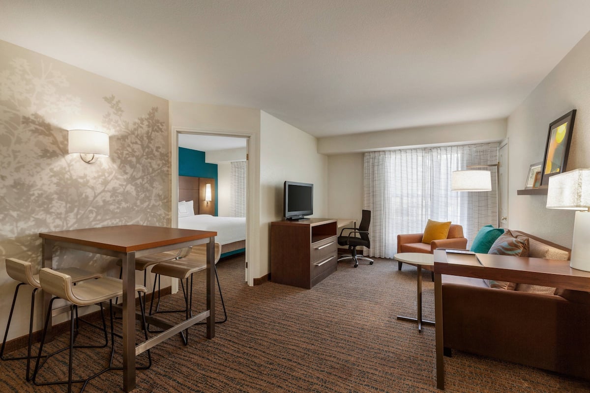 A hotel room with a dining area, a sofa, a TV, and a desk.