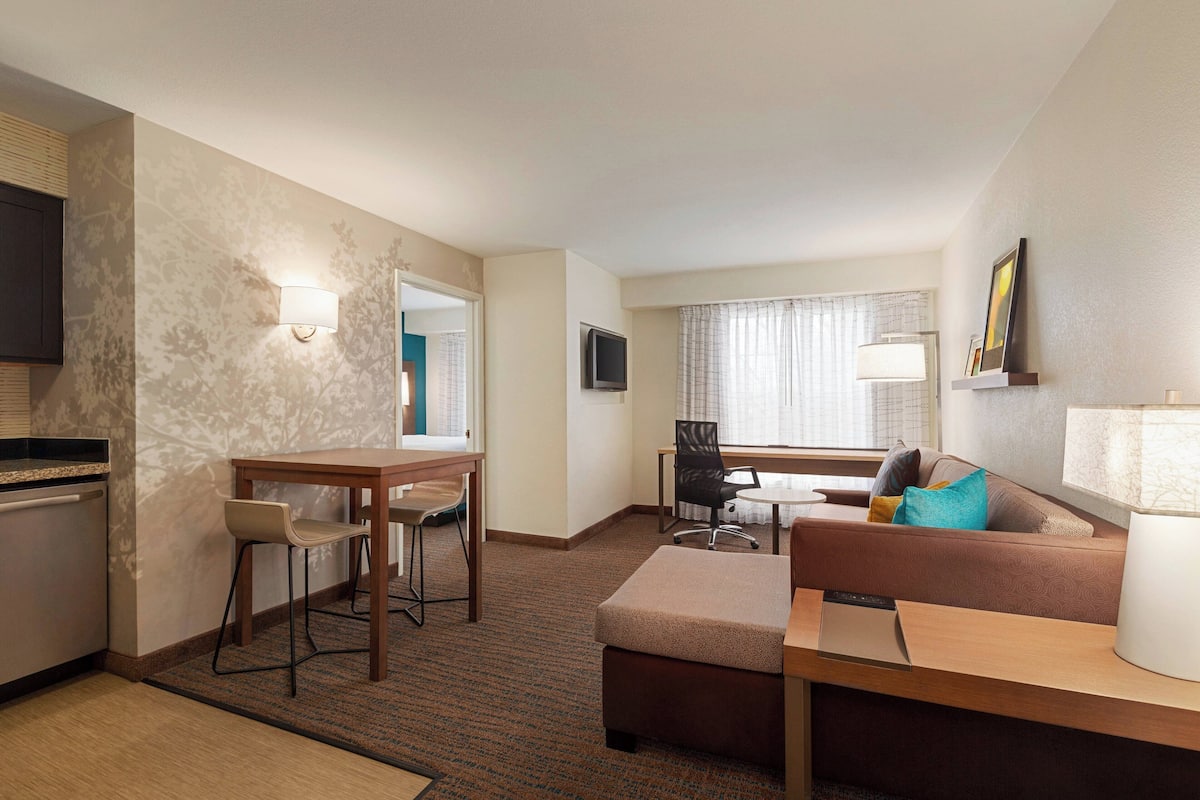 A hotel room with a kitchenette, a dining area, a sofa, and a TV.