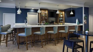 A bar area with a marble countertop, multiple bar stools, and a television mounted on the wall. - Residence Inn By Marriott Raleigh Crabtree (Raleigh)